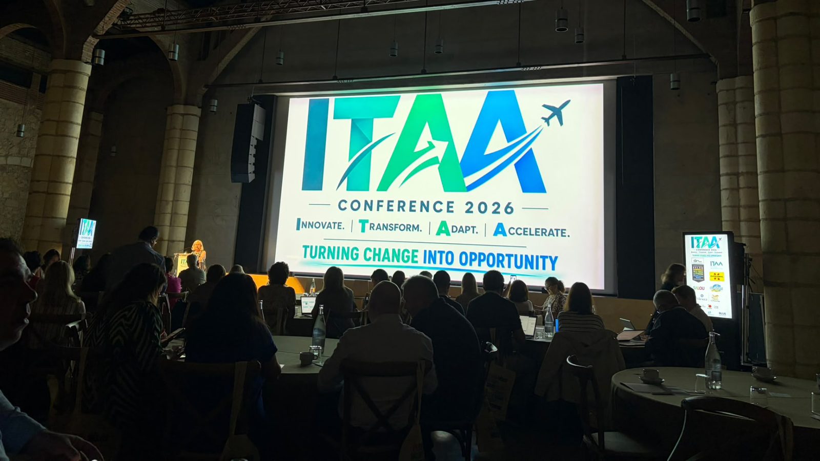 A full conference hall at Celler de Vila-seca, with delegates facing the ITAA Conference 2026 screen reading 'Turning change into opportunity'